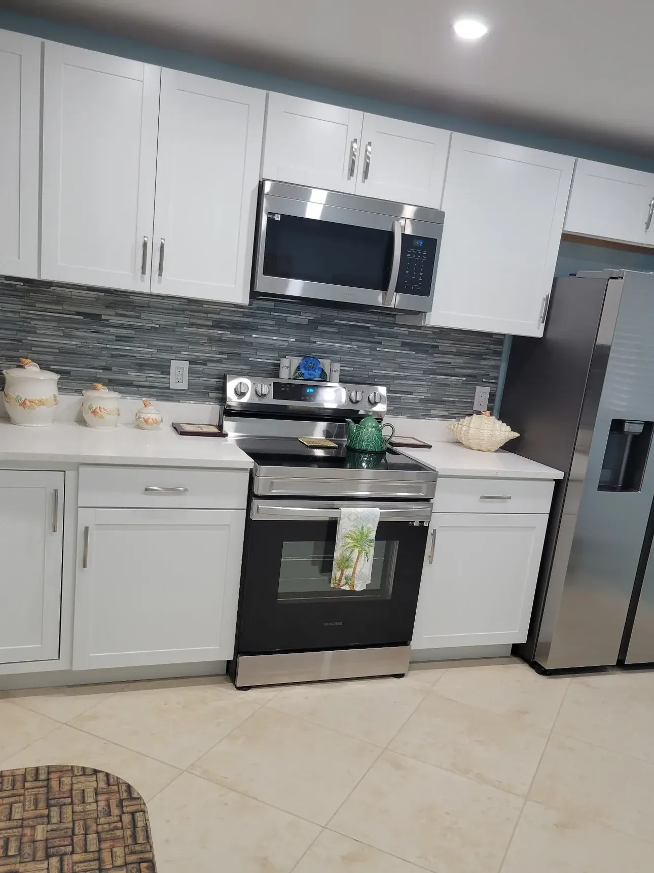 Finished kitchen with white shaker cabinets, blue-gray glass mosaic backsplash, white quartz counters and stainless appliances