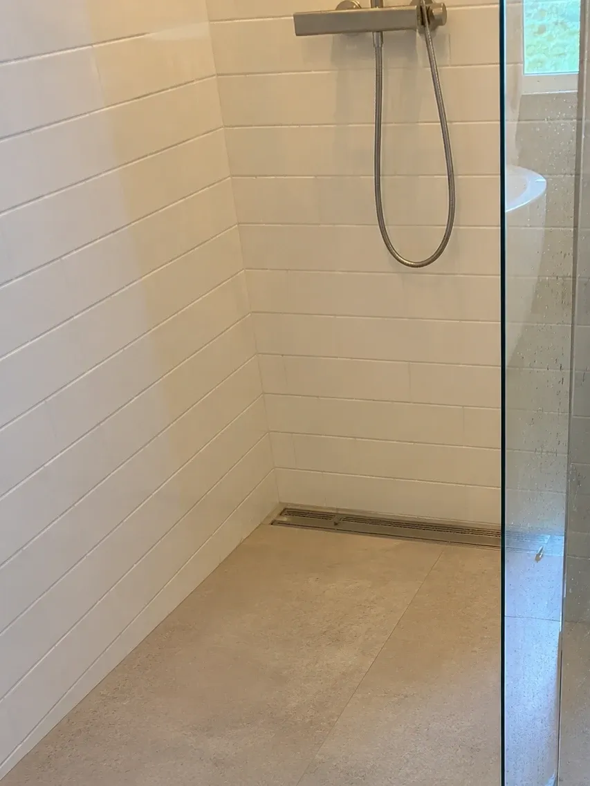 Curbless shower entry with a linear drain and tile running level from the bathroom floor into the shower