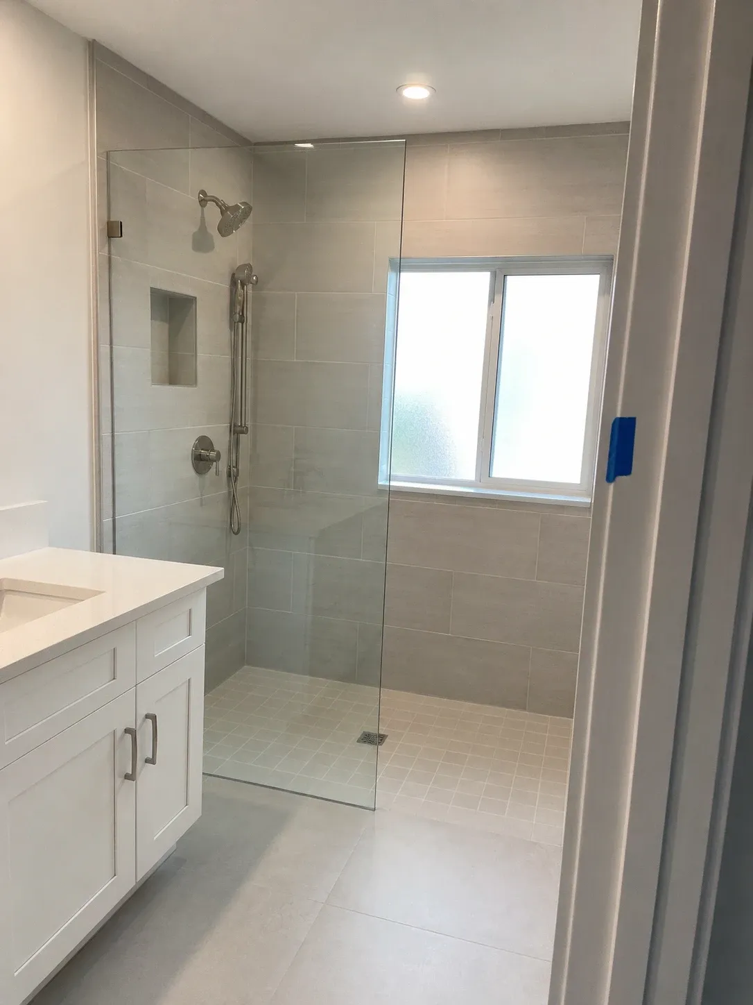 Curbless walk-in shower with a frameless glass panel, large-format tile and a white vanity with a quartz top