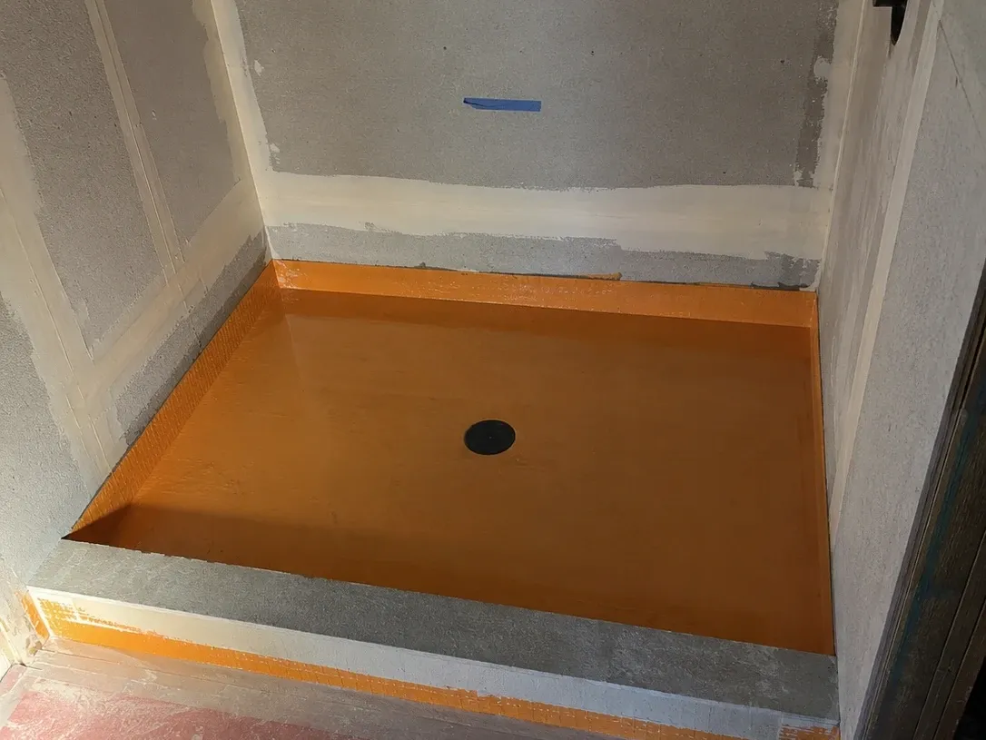 Shower pan under an overnight flood test, waterproofing membrane holding standing water before any tile goes down