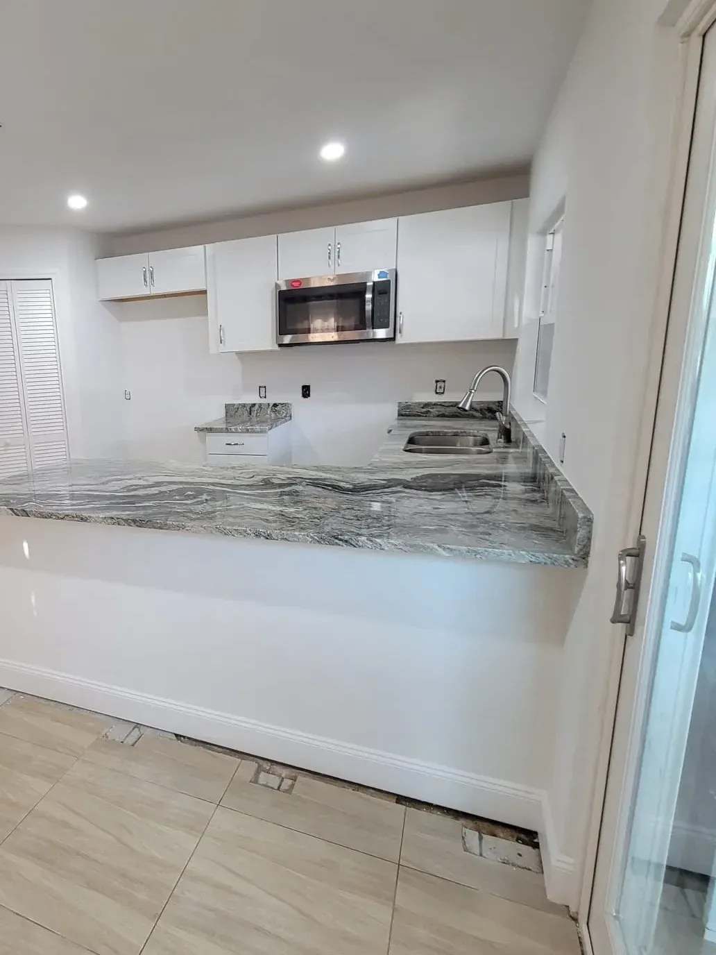 Open kitchen with a veined granite peninsula, louvered pantry door and a sliding glass door beyond