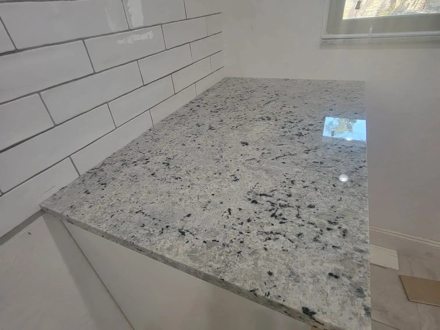 Close-up of a polished white granite countertop corner meeting a glossy white subway tile backsplash in daylight