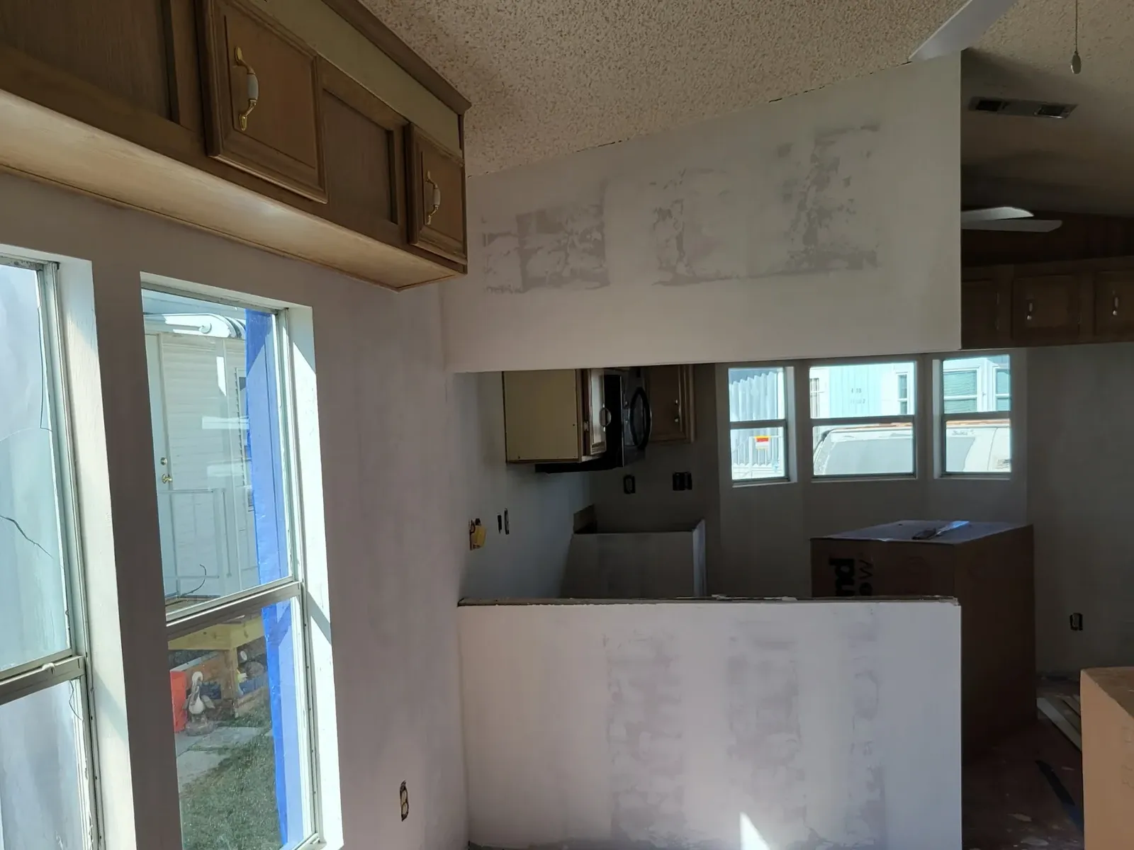 Open-plan kitchen and dining area mid-renovation with a newly drywalled half-wall, skim-coated walls and floor protection down