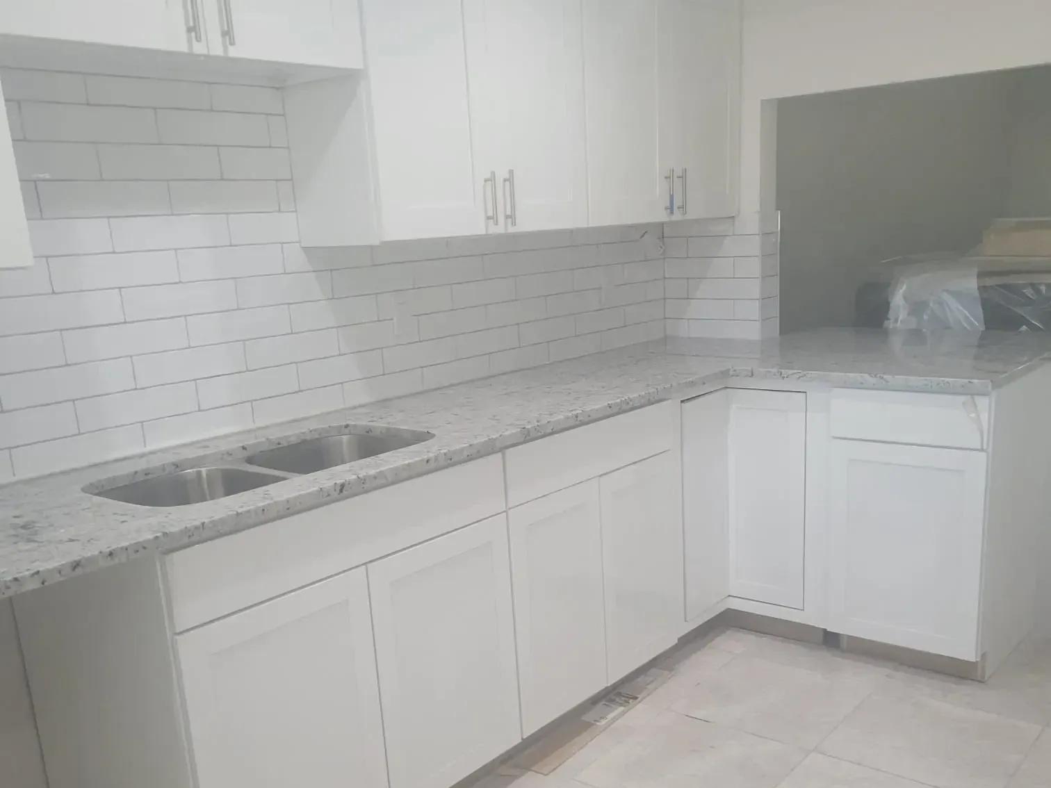 L-shaped white shaker kitchen with granite counters and subway backsplash beside a pass-through opening into the next room