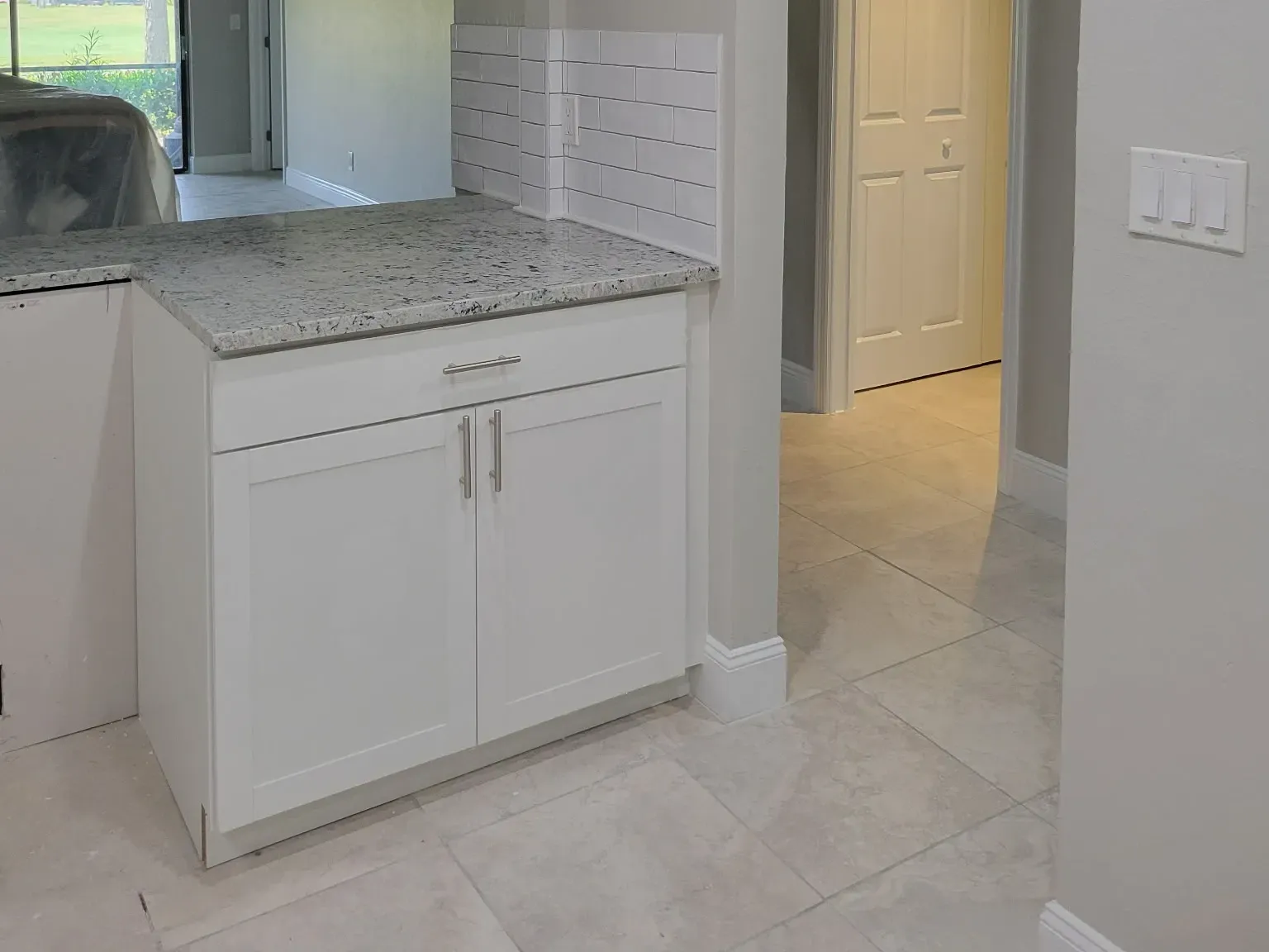 Granite-topped peninsula with a subway tile knee wall opening to a hallway and lanai view, tray ceiling and continuous tile floor