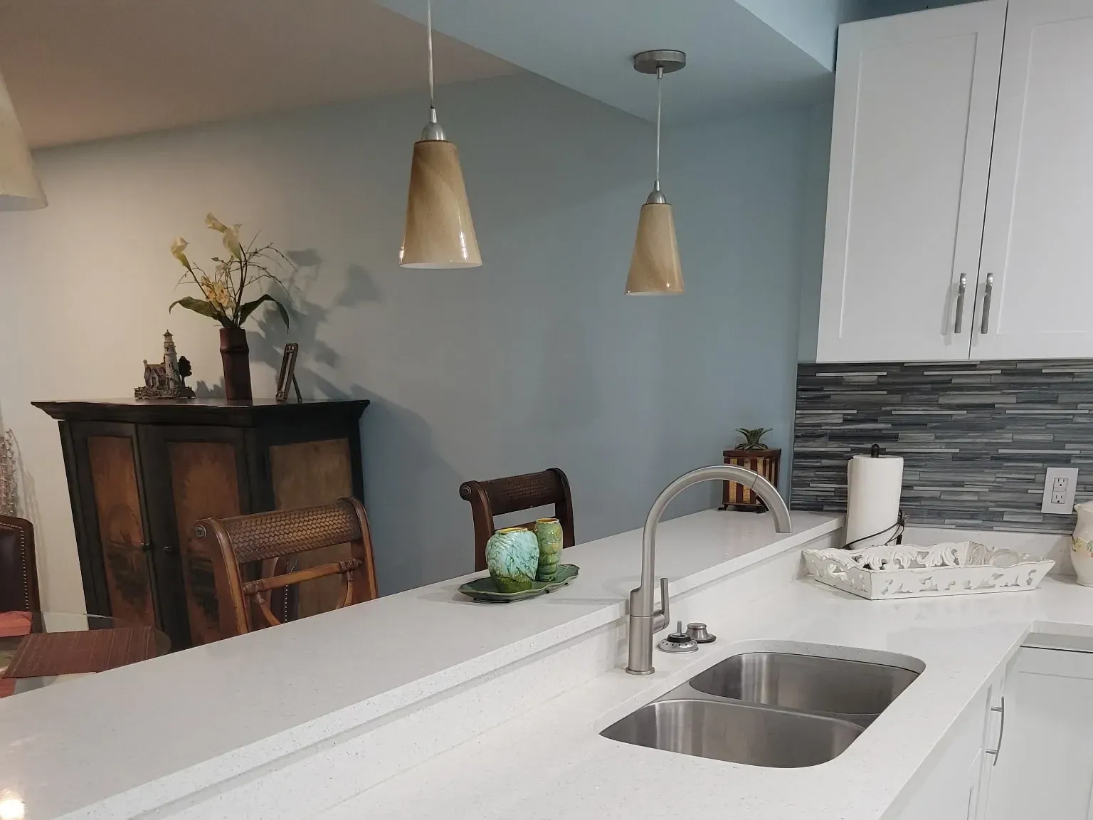 White quartz peninsula with undermount sink and gooseneck faucet under two pendant lights, open to the adjoining dining room