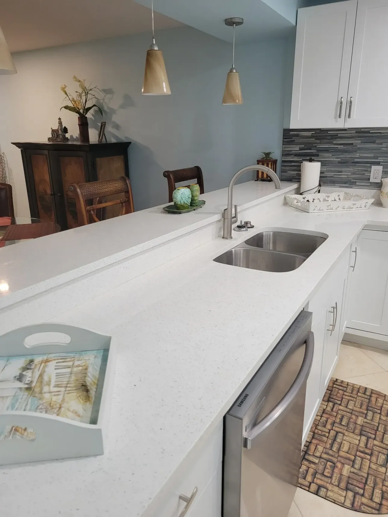 White quartz peninsula with undermount sink and gooseneck faucet under two pendant lights, open to the adjoining dining room