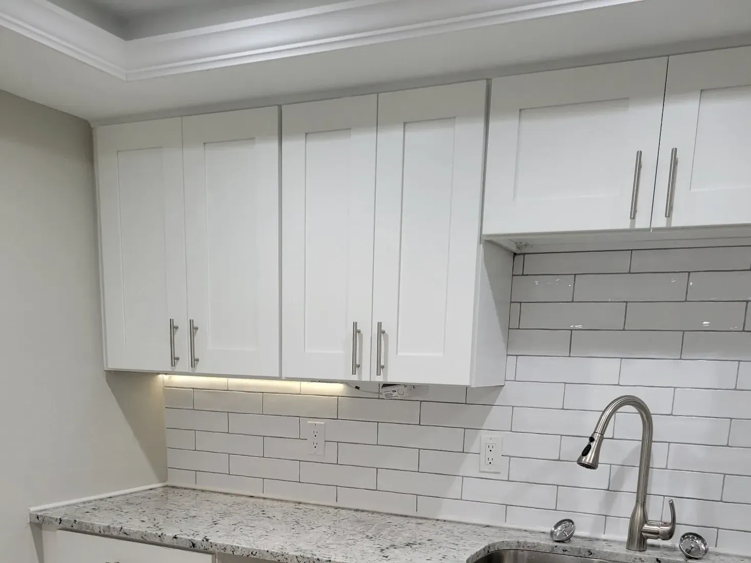 White shaker uppers with under-cabinet lighting over subway tile, granite counter and stainless double sink