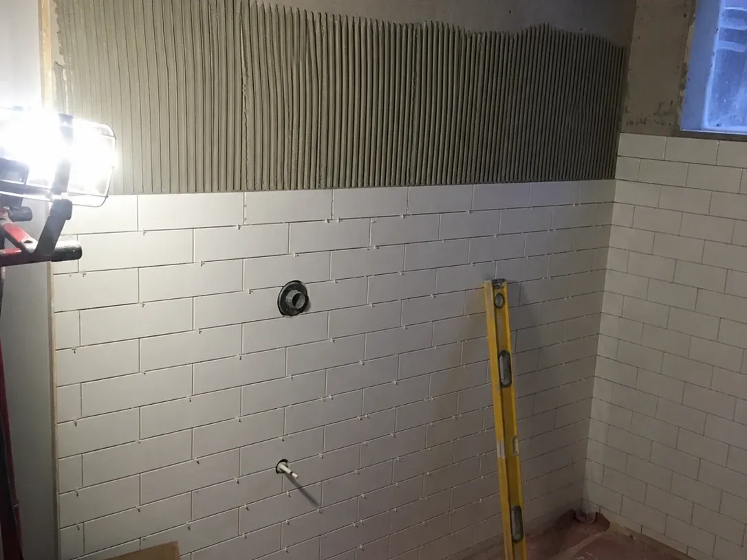 Shower walls mid-tile with spacers still set and fresh thinset ridges above the finished courses