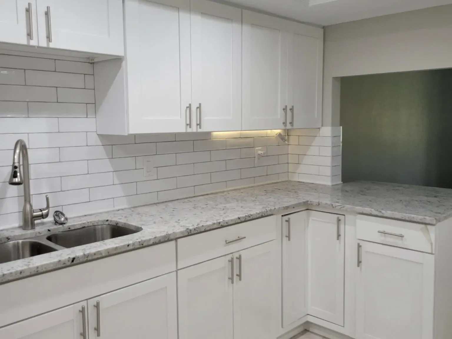 Finished white shaker kitchen with speckled granite counters, white subway tile backsplash, stainless double sink and under-cabinet lighting