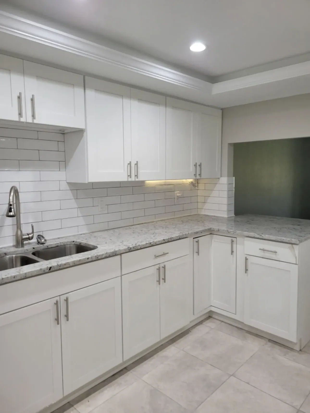 Finished white shaker kitchen with speckled granite counters, white subway tile backsplash, stainless double sink and under-cabinet lighting
